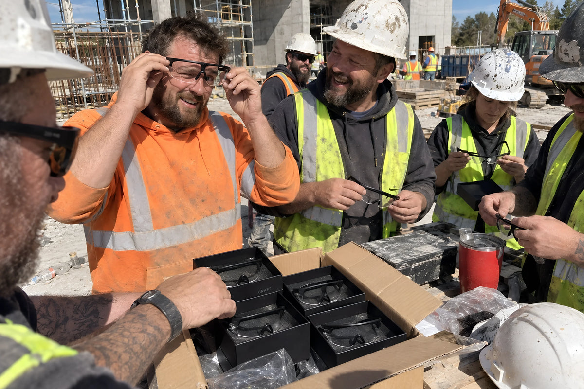 New starters on a site induction being handed clear GRAFT glasses out of the Sitebox, one already putting his on wonky. Daytime, hard sun, no candles lit.